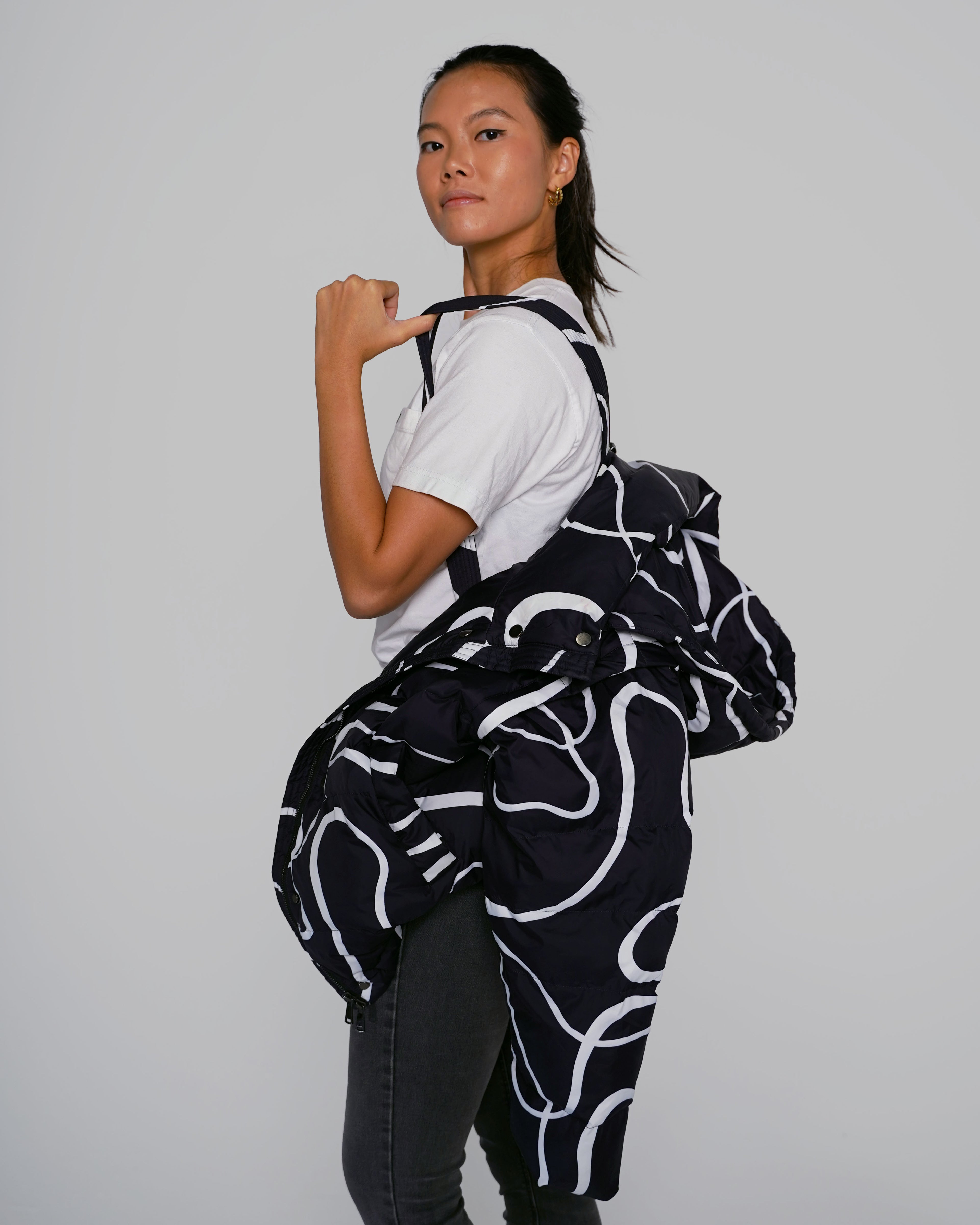 Black Wavy puffer jacket side view with adjustable straps Black Wavy streetwear puffer jacket outfit, Model wearing Black Wavy convertible puffer jacket